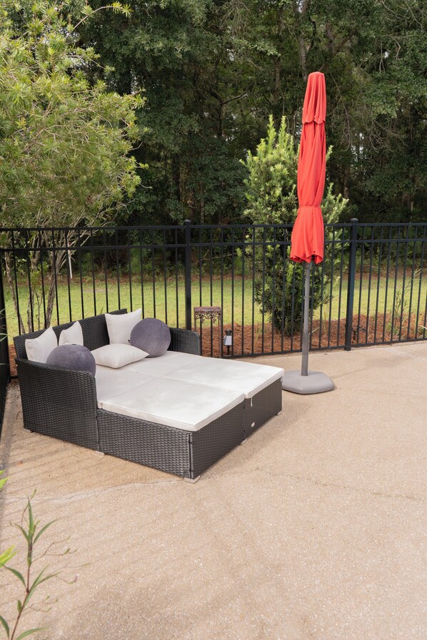 A patio with a black wicker sofa, a red umbrella, and a small table.