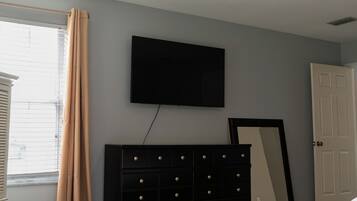 A bedroom with a bed, a dresser, a television mounted on the wall, and a ceiling fan.