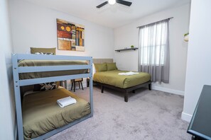 Ein Zimmer mit Etagenbetten, einem Schreibtisch, einem Stuhl, einem Vorhangfenster und einem Deckenventilator.
