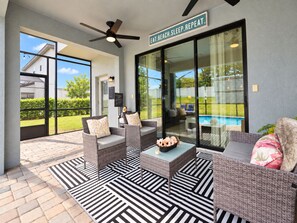 An outdoor seating area with wicker furniture, a pool in the background, and a sign that reads 'EAT. BEACH. SLEEP. REPEAT.' - Cozy Villa with Private Pool at Balmoral Resort (Haines City)