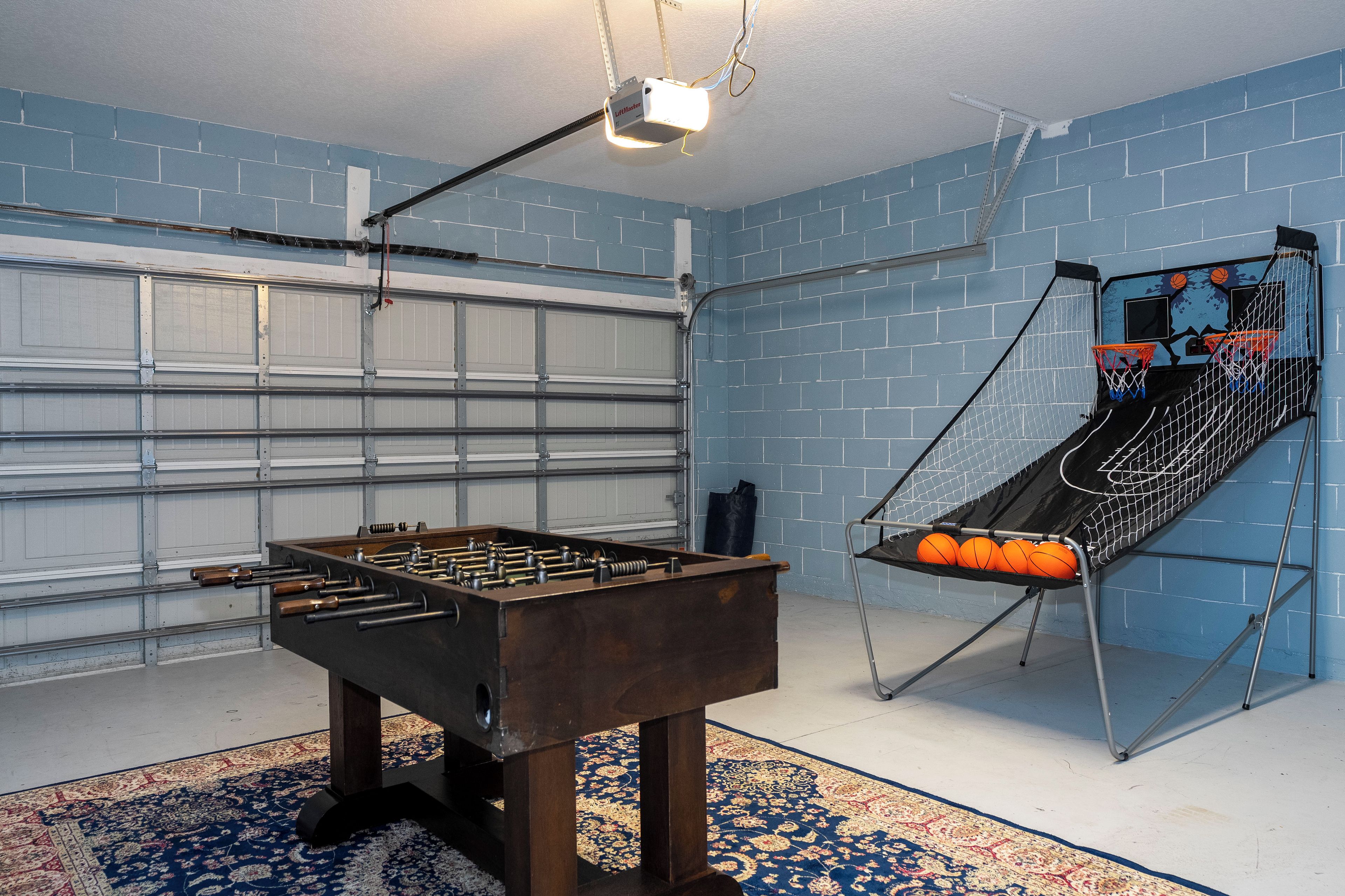 Een kamer met een tafelvoetbaltafel, een basketbalring en een garagedeur.