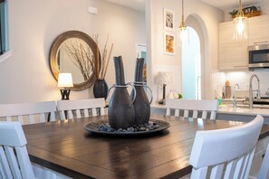 Uma mesa de jantar com dois vasos e um prato de pedras, cercada por cadeiras brancas.