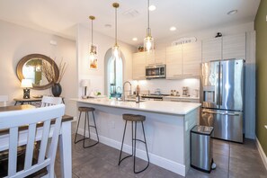 A modern kitchen with a central island, stainless steel appliances, pendant lighting, and a dining area with a white table and chairs. - Cozy Villa with Private Pool at Balmoral Resort (Haines City)