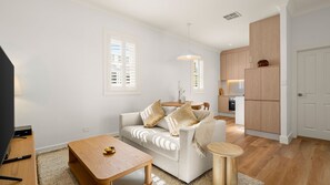 Ein modernes Wohnzimmer mit einer Couch, einem Couchtisch und einem kleinen Beistelltisch. Es gibt eine Küchenzeile mit Holzschränken und einem Kühlschrank.