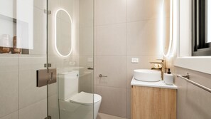 Ein modernes Badezimmer mit einer gläsernen Duschkabine, einer weißen Toilette und einem Waschtisch mit Waschbecken und Spiegel.
