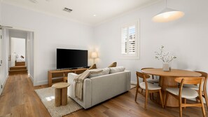 A modern living room with a flat-screen TV, a sofa, a dining table with chairs, and a small round side table. - The Short Story Randwick - Unit 1 (Randwick)