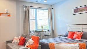 Quarto moderno com cama, sofá, ventilador de teto e janela com cortinas.