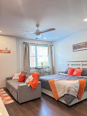 Un dormitorio moderno con cama, sofá, ventilador de techo y ventana con cortinas.