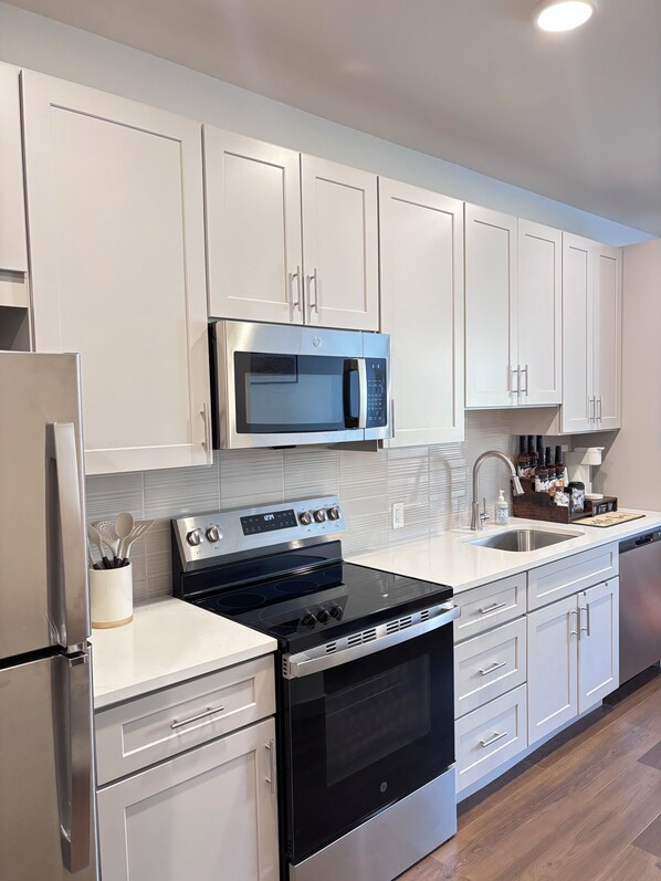 A modern kitchen with stainless steel appliances, white cabinetry, and a wooden floor.