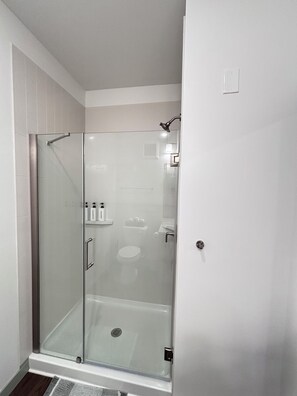 Un baño moderno con ducha envuelta en vidrio, paredes de azulejos blancos y un inodoro a la vista.