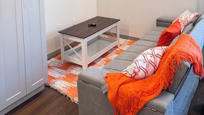 Uma sala de estar moderna com um sofá cinza, uma mesinha e uma TV fixada na parede.