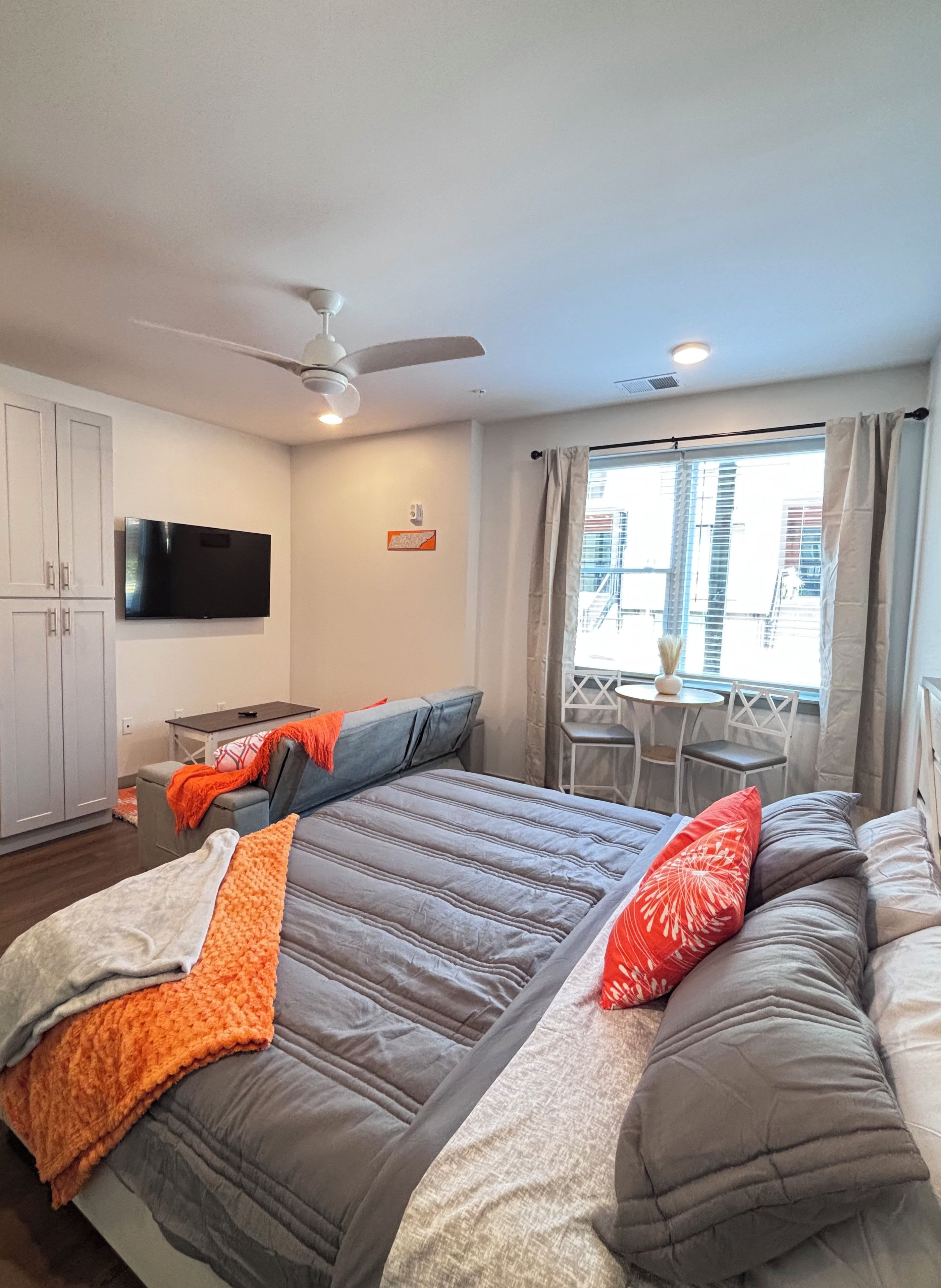A hotel room with a bed, a TV, a ceiling fan, and a window with curtains.