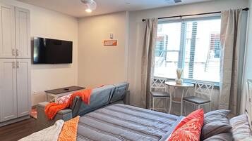 A hotel room with a bed, a TV, a ceiling fan, and a window with curtains.