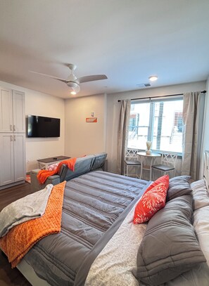 A hotel room with a bed, a TV, a ceiling fan, and a window with curtains.