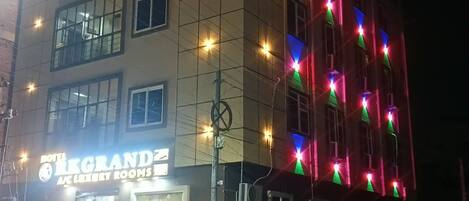 A hotel building with multiple floors, a sign indicating 'Hotel Grand,' and a parked white car in front.