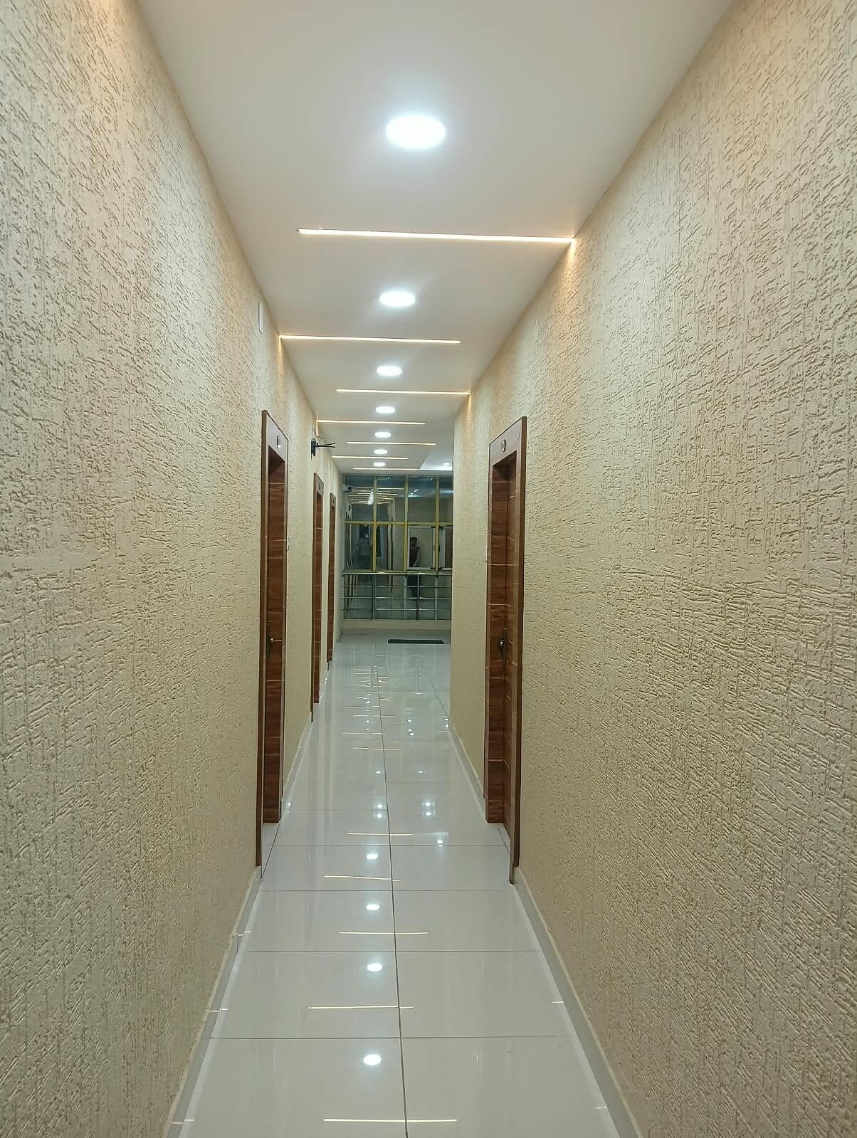 Un pasillo con pared texturizada, piso de baldosas brillantes y luces empotradas en el techo.