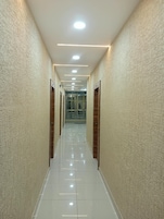 Un pasillo con pared texturizada, piso de baldosas brillantes y luces empotradas en el techo.