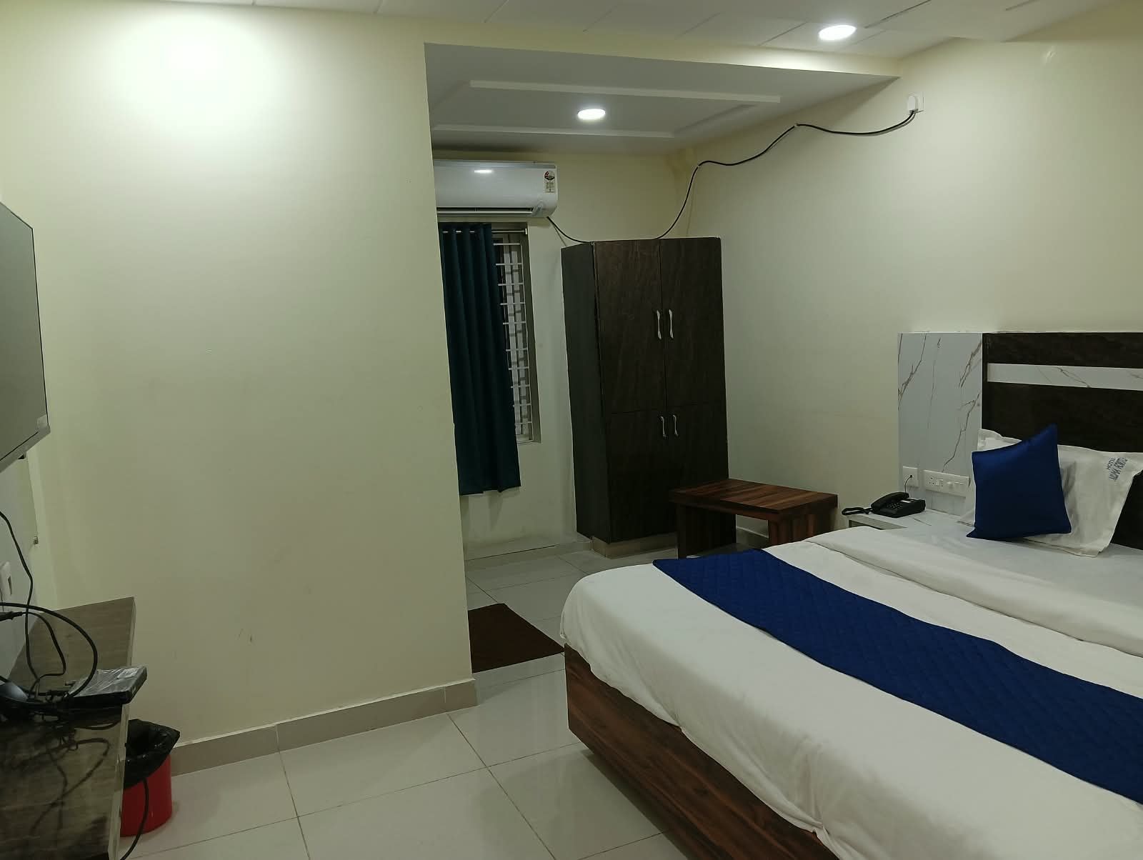Quarto de hotel com cama, guarda-roupa, secretária com telefone e televisão.