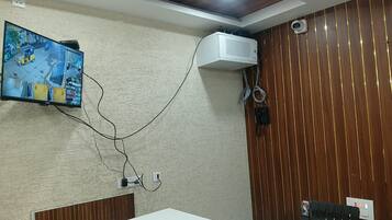 A conference room with a white table, a television mounted on the wall displaying a street view, and a ceiling fan.