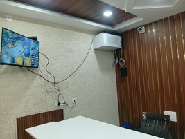 Un salón de conferencias con una mesa blanca, un televisor en la pared mostrando una vista de la calle y un ventilador de techo.