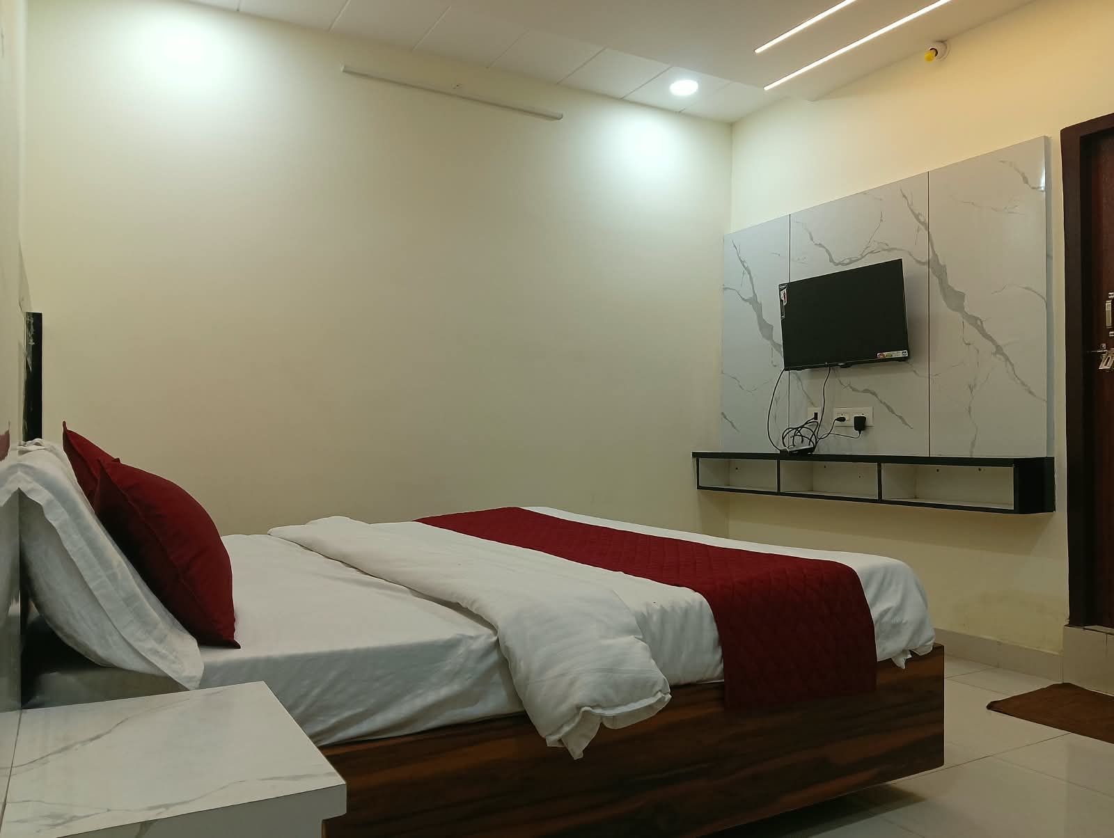 A hotel room with a bed, a TV mounted on the wall, and a wooden nightstand.
