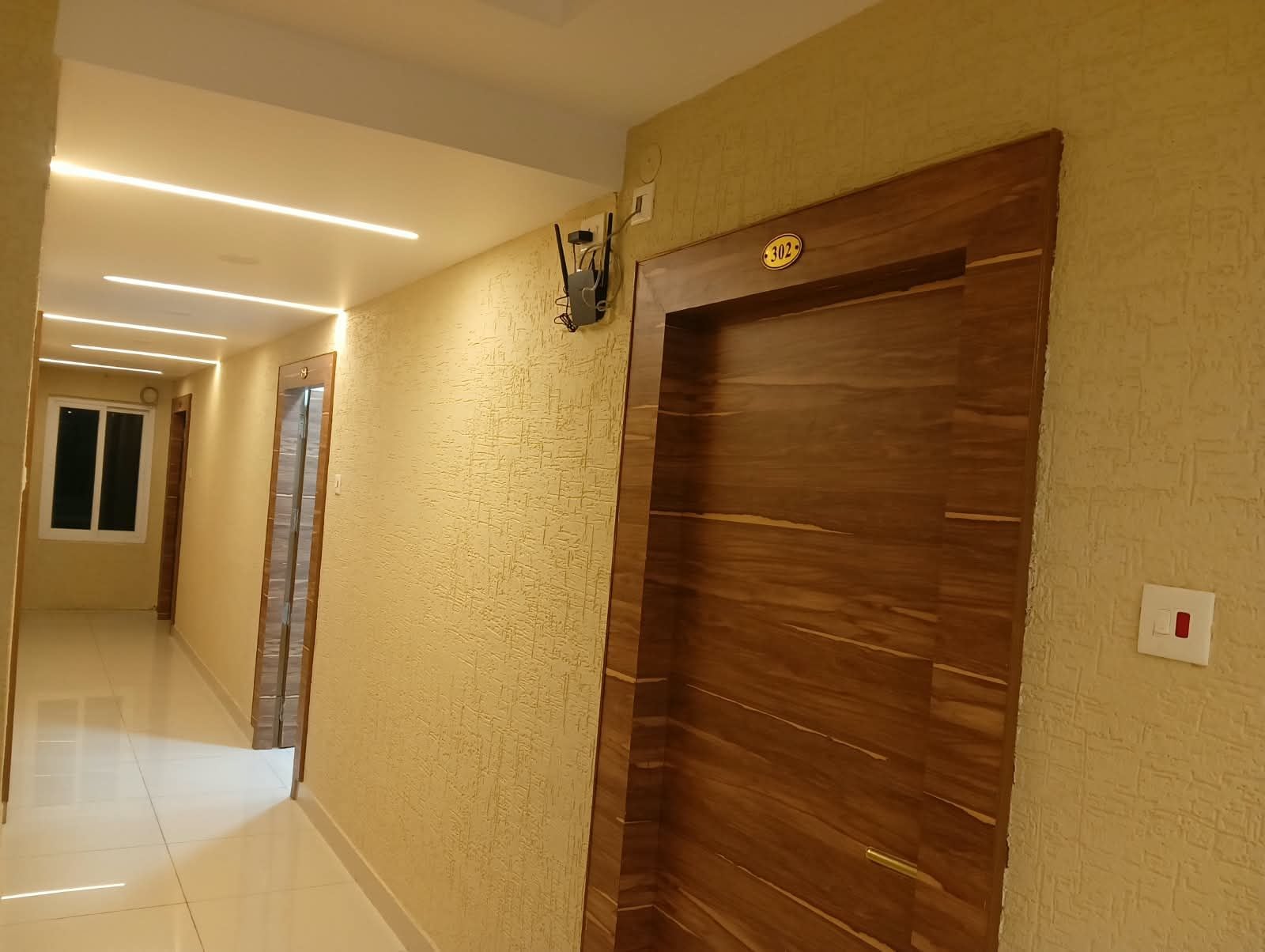 A hallway with a wooden door, a wall-mounted light fixture, and a tiled floor.