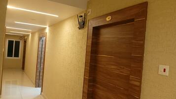 A hallway with a wooden door, a wall-mounted light fixture, and a tiled floor.