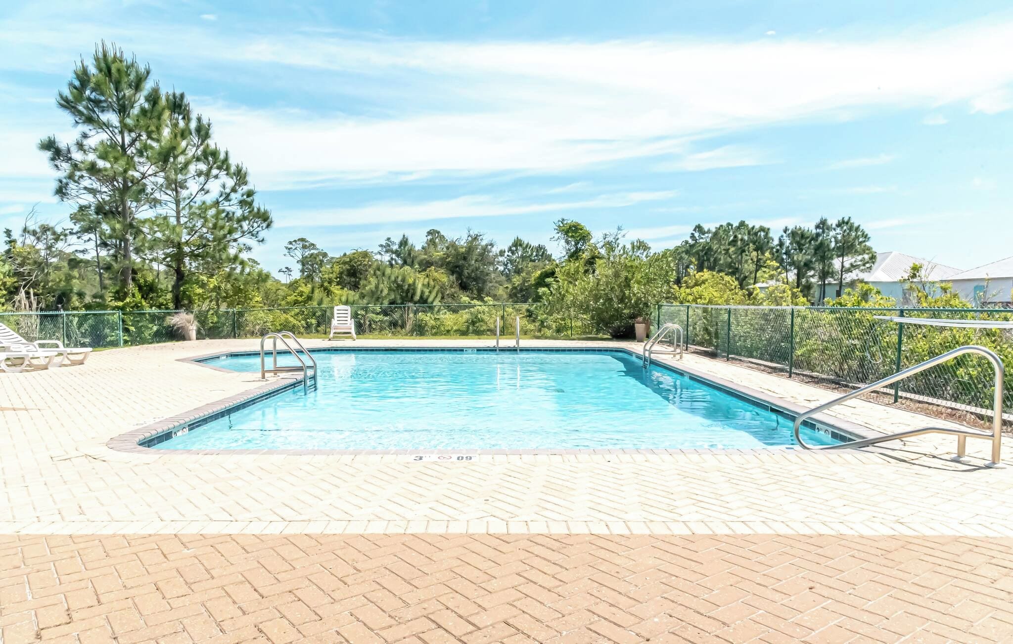Une piscine rectangulaire avec une terrasse carrelée, entourée d’une clôture, et sur laquelle on peut apercevoir un seul fauteuil de relaxation.