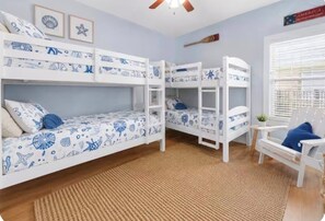 Ein Zimmer mit Etagenbetten, einem Deckenventilator, einem Fenster mit Jalousien und einem Stuhl.
