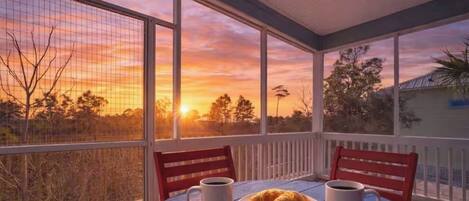 Un patio techado con una mesa dispuesta para el desayuno, con vista a una puesta de sol.