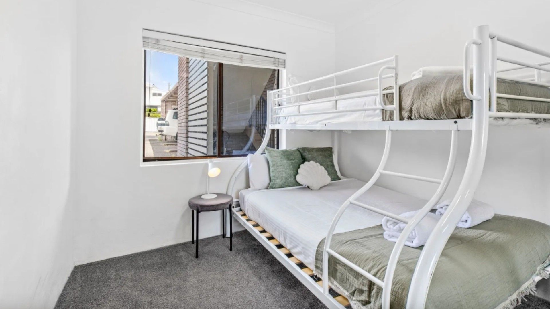 Une chambre avec un lit superposé, une fenêtre, une petite table et une lampe.
