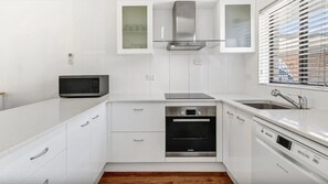 A modern kitchen with white cabinetry, a microwave, a built-in oven, and a dishwasher. - Surf's Up Sawtell - Walking Distance To Beach and Cafes (Sawtell)
