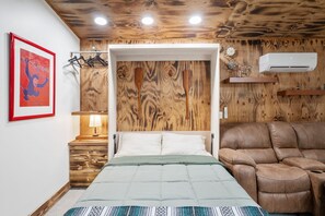 A bedroom with a wooden ceiling, a bed with a green and white duvet, a brown leather chair, a wooden nightstand with a lamp, and a framed picture on the wall. - HOPEWELL OASIS - TAMPA / Your Private Wellness Retreat with Hot Tub & Sauna (Tampa)