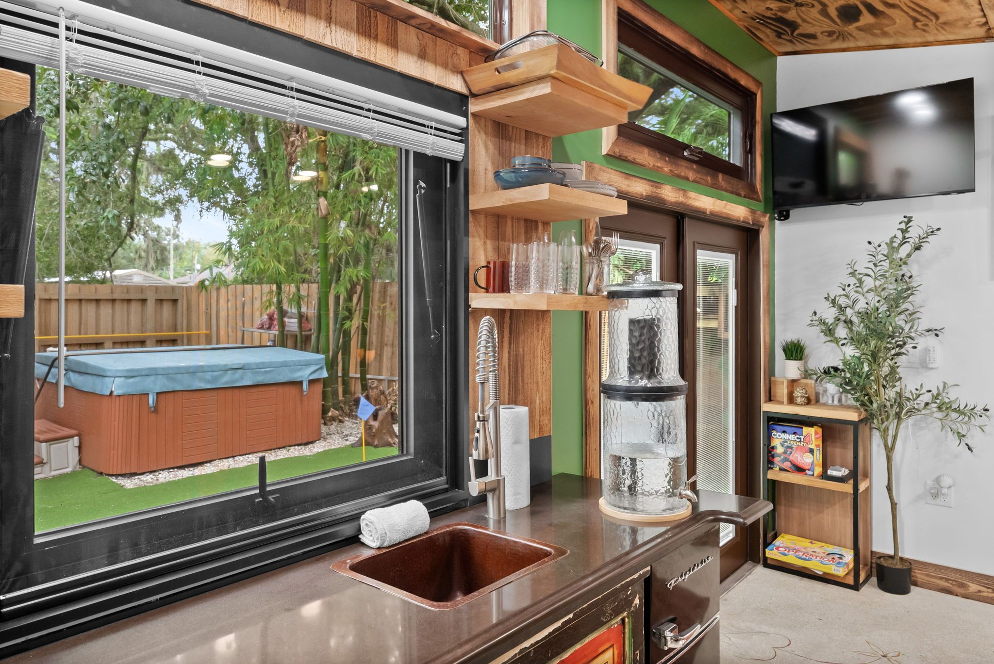 A modern kitchen with a large window, wooden shelves, a built-in sink, and a small indoor garden.