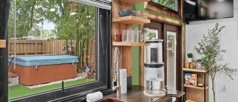 A modern kitchen with a large window, wooden shelves, a built-in sink, and a small indoor garden.