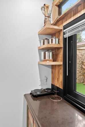 Uma cozinha com prateleiras de madeira com panelas e frigideiras, bancada com chaleira e janela com vista para o exterior.