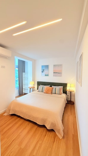A modern bedroom with a large bed, bedside lamps, a built-in shelf, and a window with curtains. - Modern 1 bedroom apartment in the heart Cascais with AC, amenities (Cascais)