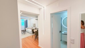 A modern hotel room with a wooden floor, a bed, a desk, and a bathroom with a mirror. - Modern 1 bedroom apartment in the heart Cascais with AC, amenities (Cascais)
