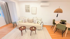 Ein modernes Wohnzimmer mit einer Couch, zwei Beistelltischen, einem Esstisch mit Stühlen und Kunstwerken an den Wänden.