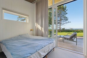 Een slaapkamer met een bed, een raam en uitzicht op een terras en de omgeving.