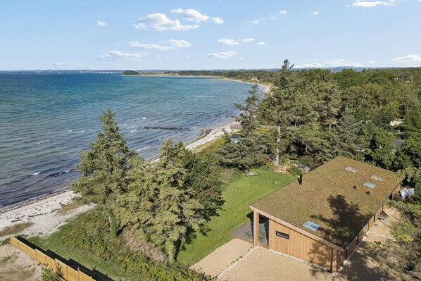 Een landhuis aan de kust met een houten huisje, een gazon en een strand.