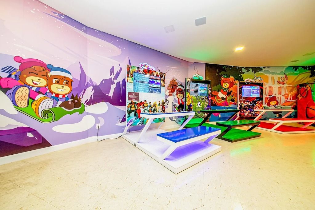 Espaço de recreação infantil com murais coloridos, estações de jogos e assentos.