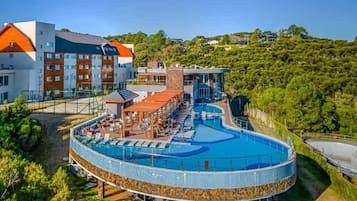 Un resort con una amplia piscina circular, una zona de estar cubierta y un edificio de varios pisos.