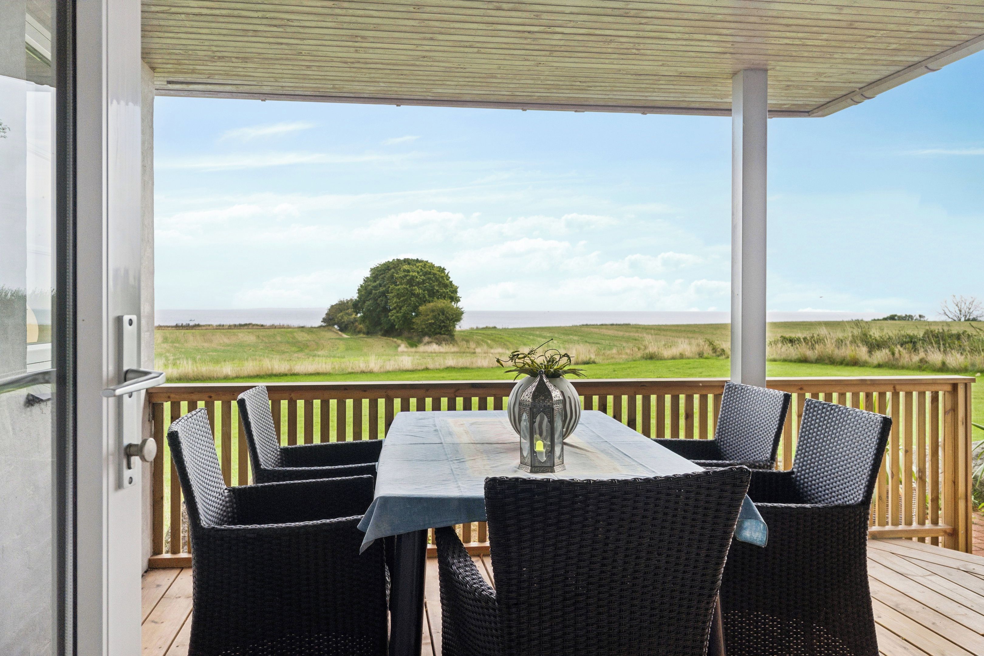 Een terras buiten met een tafel, stoelen, een lantaarn en uitzicht op een grasveld en een boom.