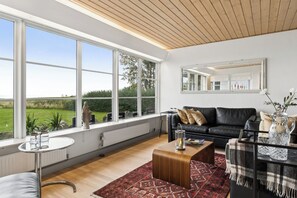 A modern living room with a large window, a black leather sofa, a wooden coffee table, and a patterned rug. - Holiday home near the water on beautiful Als (Augustenborg)