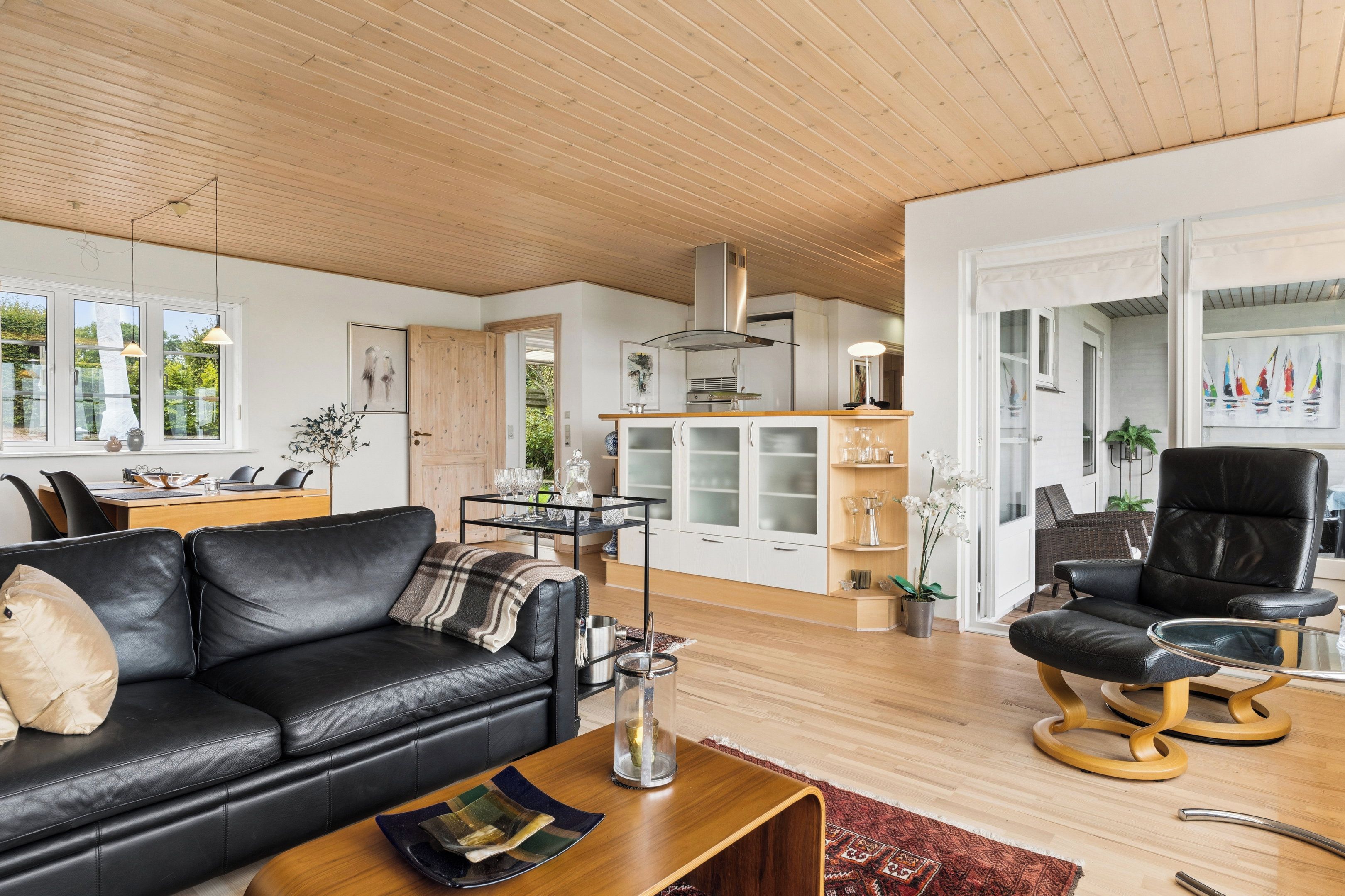A modern living room with a black leather sofa, a wooden coffee table, and a dining area with a wooden table and chairs.