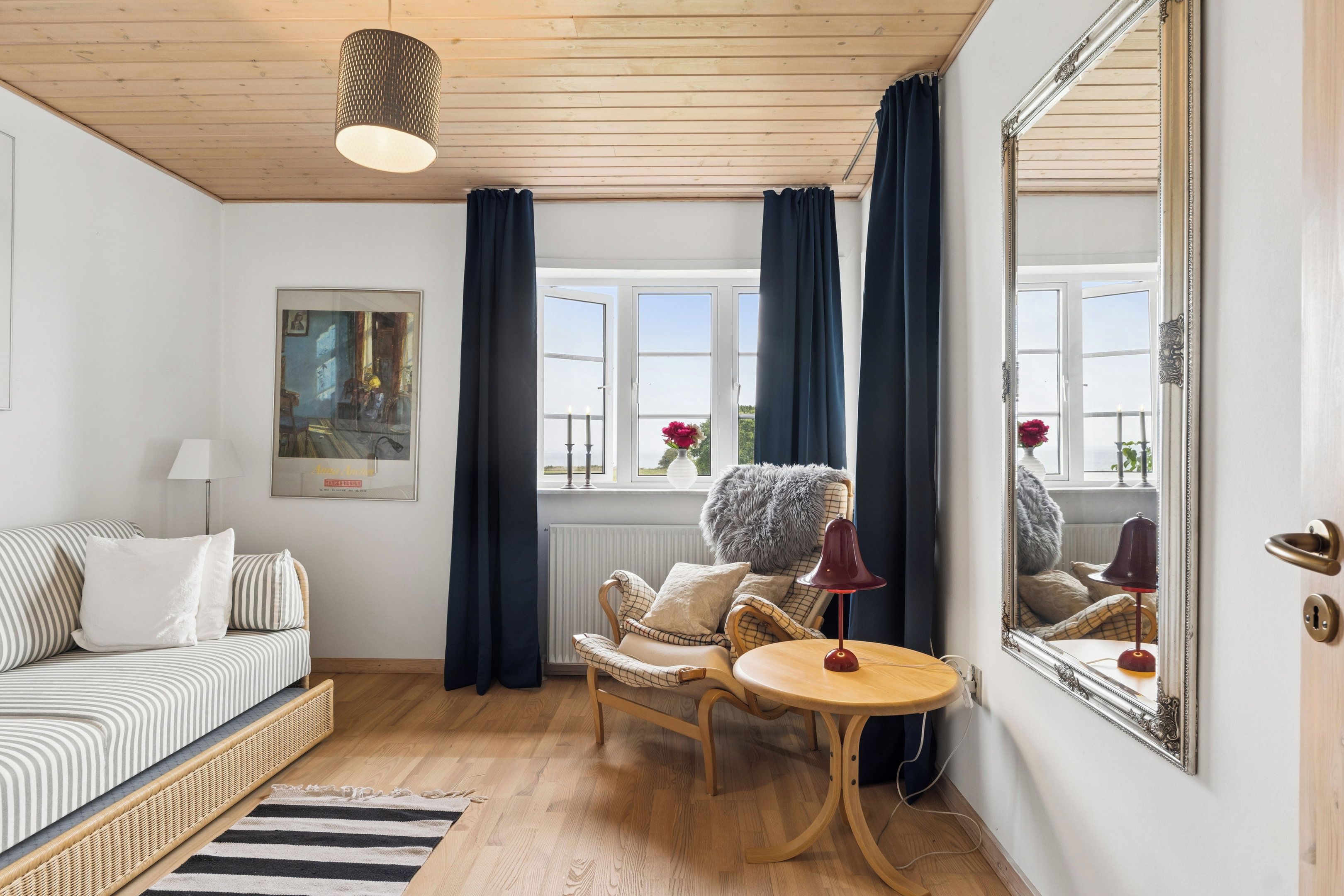 Ein gemütliches Zimmer mit einer Couch, einem Sessel, einem runden Tisch, einem Spiegel und einem Fenster mit Vorhängen.
