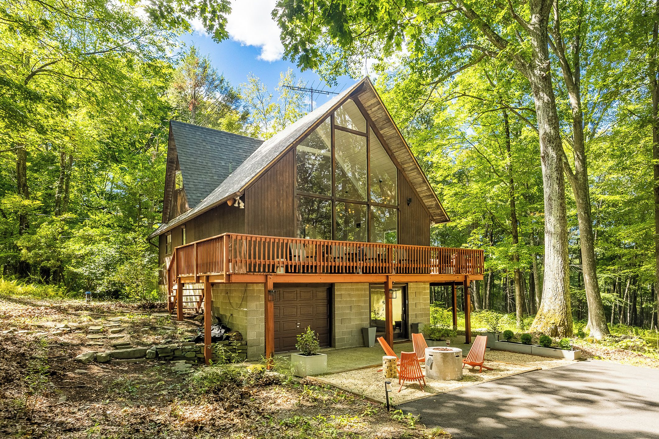 A cabin with a large glass front, wooden deck, and a stone foundation.