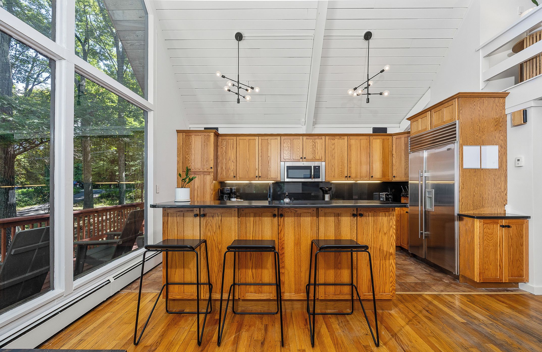 Une cuisine moderne avec des meubles en bois, des appareils électroménagers en acier inoxydable et une grande fenêtre donnant sur une terrasse.