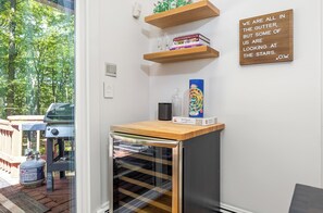 Eine kleine Küche mit integriertem Minikühlschrank, einer Holz Arbeitsplatte und einem Regal mit Büchern und Gläsern.